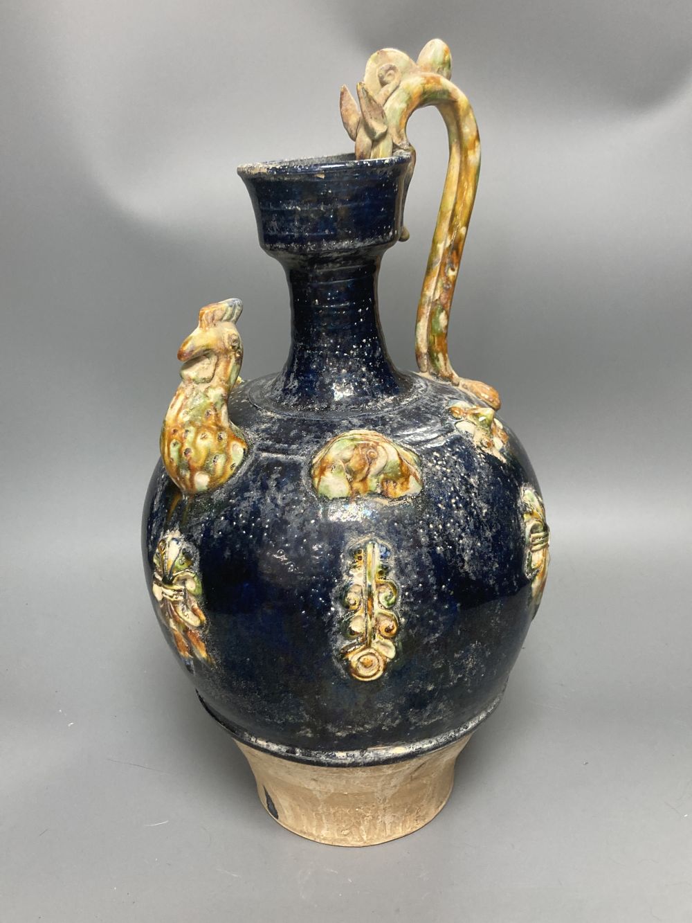 A group of Chinese Tang style pottery figures, tallest 28cm and a partially glazed ewer in sancai colours against a blue ground, 40cm